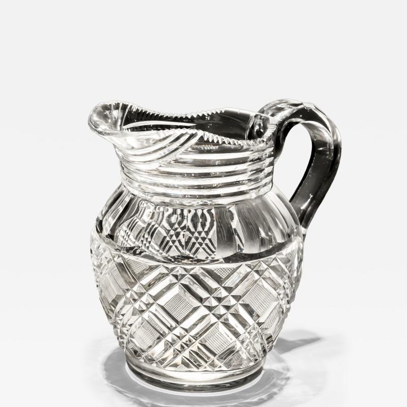 A HEAVILY CUT GLASS CREAM JUG