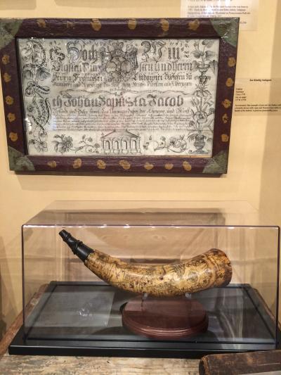 In the booth of Jennifer and Joe Kindig, A German fraktur hangs above an extraordinary powder horn from the French and Indian War; the detailed, engraved scene depicts New York. 