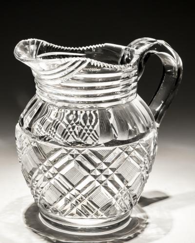 A HEAVILY CUT GLASS CREAM JUG