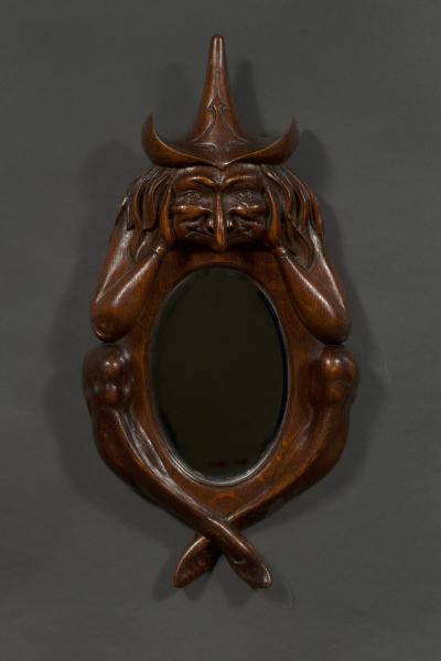 An oval arts and crafts period carved oak scrying mirror in the form of a witch